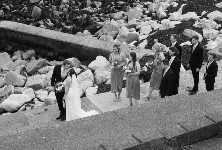 Black and white shot of couple kissing on pier with party behind them